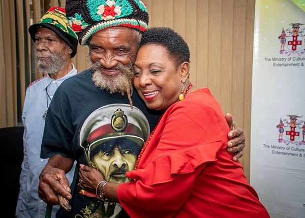 The Minister of Culture, Gender, Entertainment and Sport, the Honourable Olivia Grange, embraces Edward Fray, a survivor of the 1963 Coral Gardens incident, after the formal establishment of the Trust in December 2019. Also pictured is Isaac Wright, another survivor.